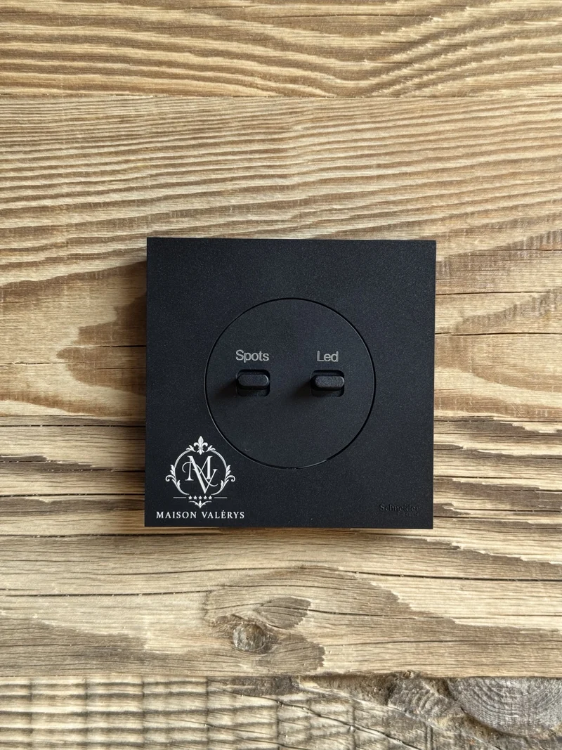 Plaque noire avec commandes Spots et Led et logo Maison Valérys gravé, sur un fond bois.