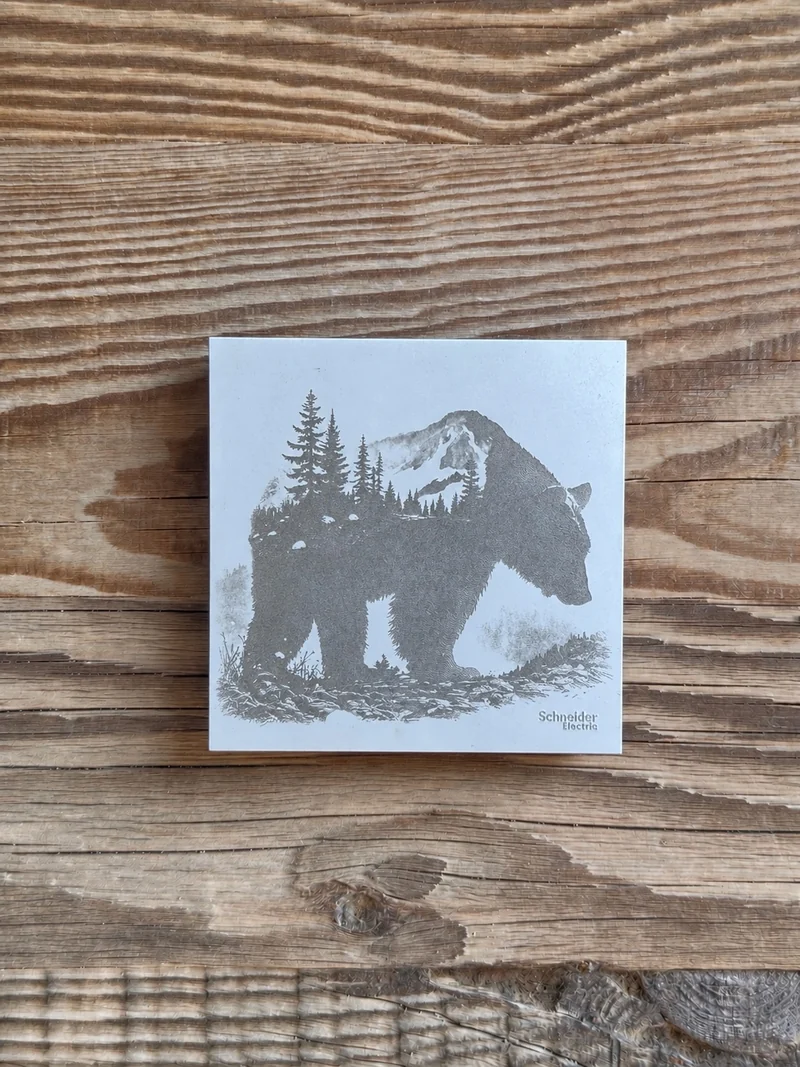 Ours, forêt et montagne gravés sur une plaque claire présentée sur du bois.