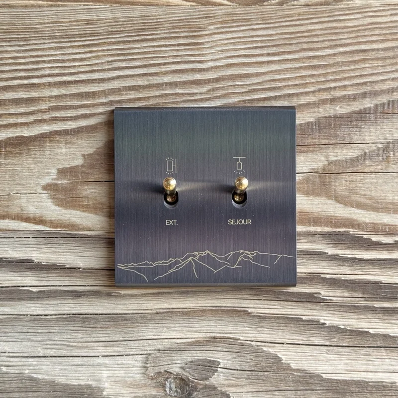 Plaque noire à deux commandes avec les lignes de montagne gravées, sur un mur en bois.