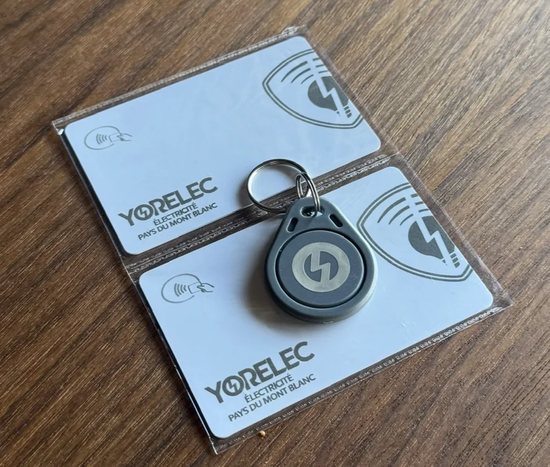 Deux badges et un porte-clés personnalisés avec le logo Yorelec, posés sur une table en bois.