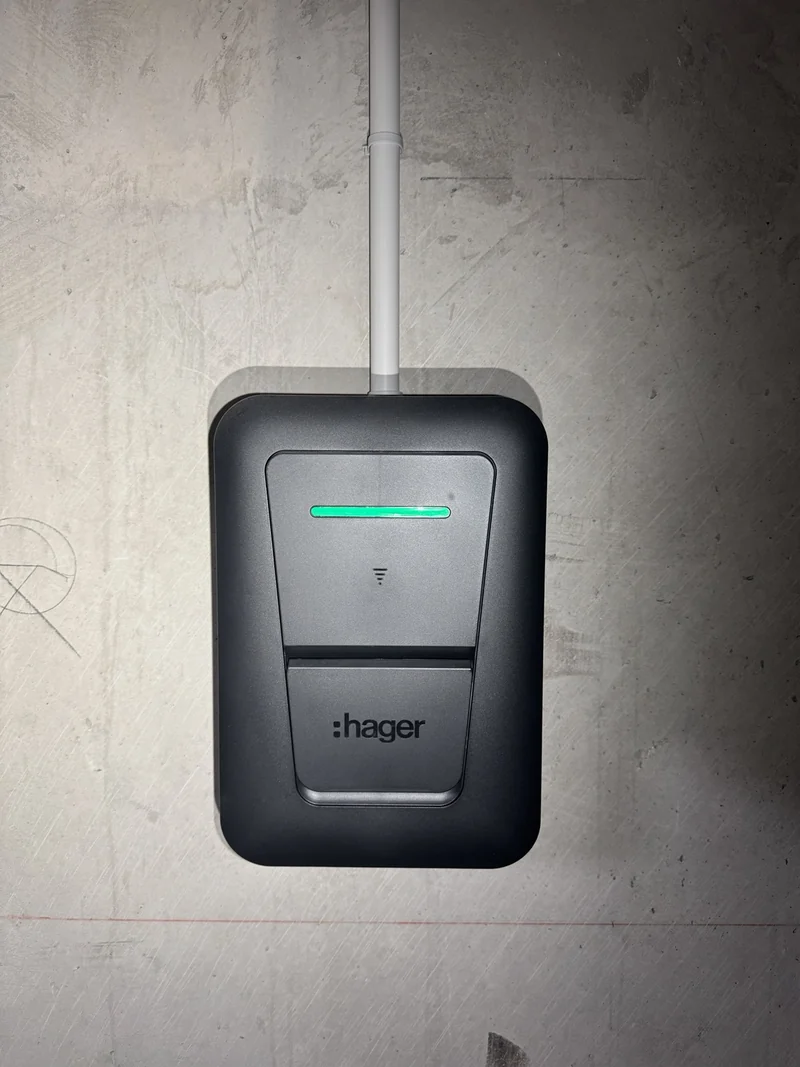 Borne Hager Witty One installée sur un mur gris, avec arrivée électrique par le haut.